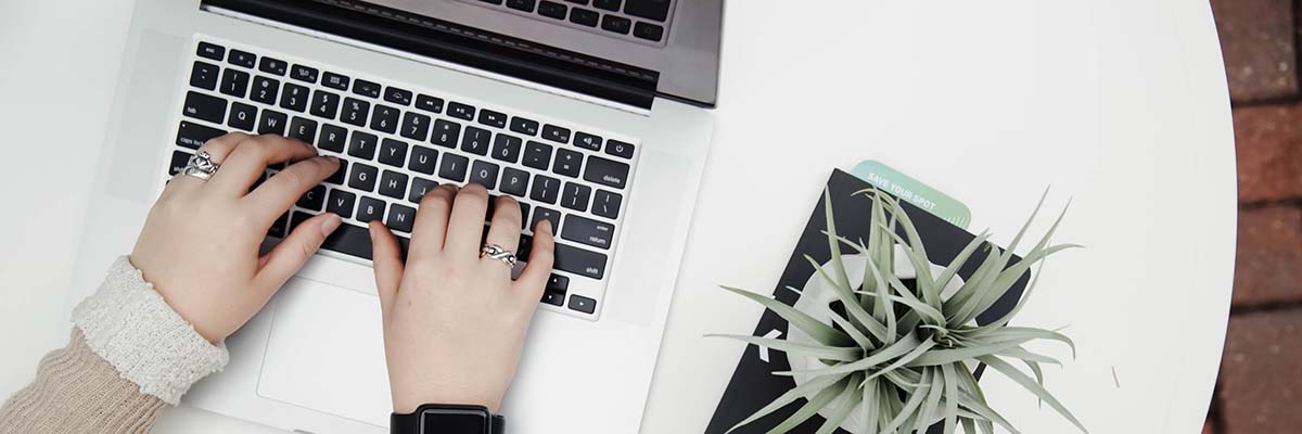 close up of person typing on laptop next to small fern on round white table