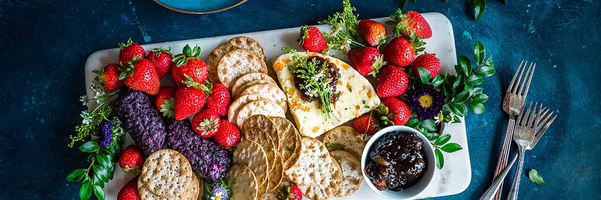 various crackers with strawberries, white cheese and blackberry jam on large white rectangular serving dish