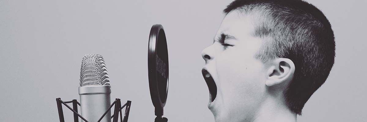 Boy yelling into podcast booth microphone