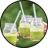 3 green smoothies in glass mason jars with handles and straws being cheered