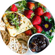 various crackers with strawberries, white cheese and blackberry jam on large white rectangular serving dish