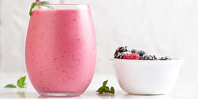 glass with pink protein shake and small bowl of berries