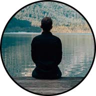 man with back to us looking at scenic lake surrounded by lush green plant covered mountains