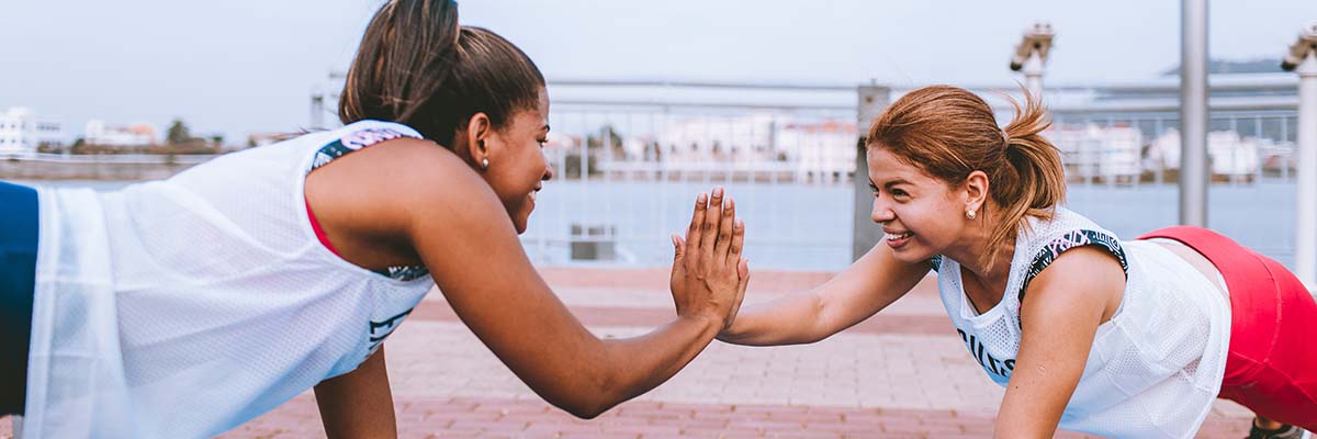 two women smiling and high fiving while each is doing a push-up