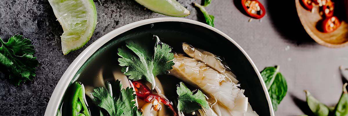 skillet of fish and vegetables surrounded by lime and red jalapeno peppers