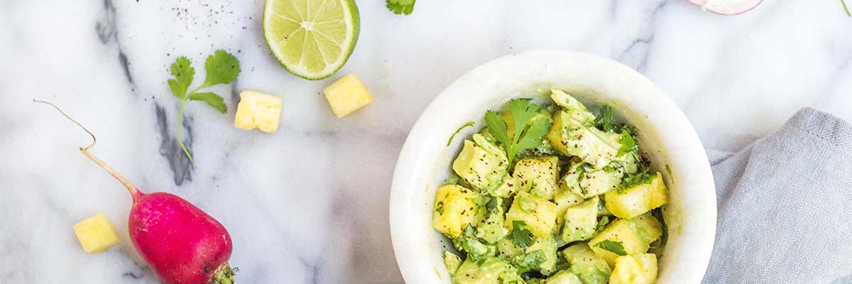 bowl of green and yellow vegetables with lime and radish to the side